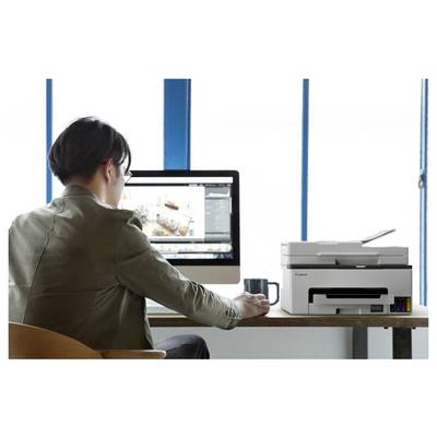 Eine Person, die an einem Desktop-Computer neben einem Drucker in einem hellen Büro arbeitet, von hinten betrachtet.