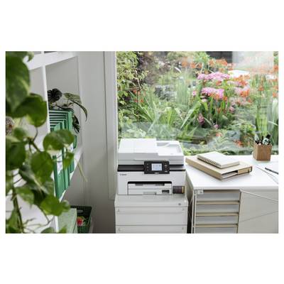 Homeoffice-Ecke mit einem Canon-Drucker neben einem Schreibtisch an einem Fenster mit Ausblick auf einen üppigen Garten mit rosa Blüten.
