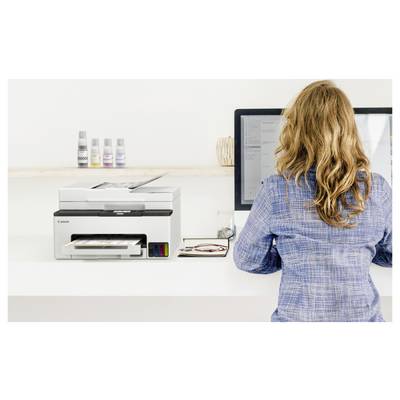 Frau, die neben einem Canon-Drucker an einem Computer in einem Büro oder Druckladen steht und ein Dokument auf dem Bildschirm ansieht.