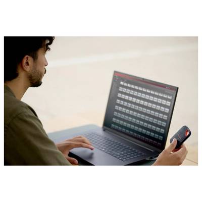 Mann mit einem Laptop, der ein Smartphone in der Hand hält und ein Raster von Dateien oder Miniaturansichten auf dem Laptop-Bildschirm überprüft.
