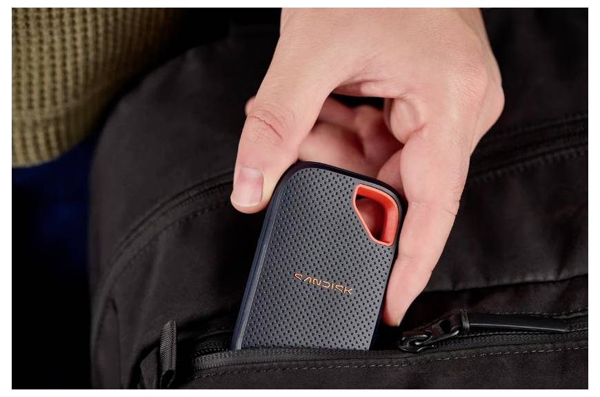 Hand, die eine tragbare externe SanDisk SSD in eine schwarze Taschentasche einführt.