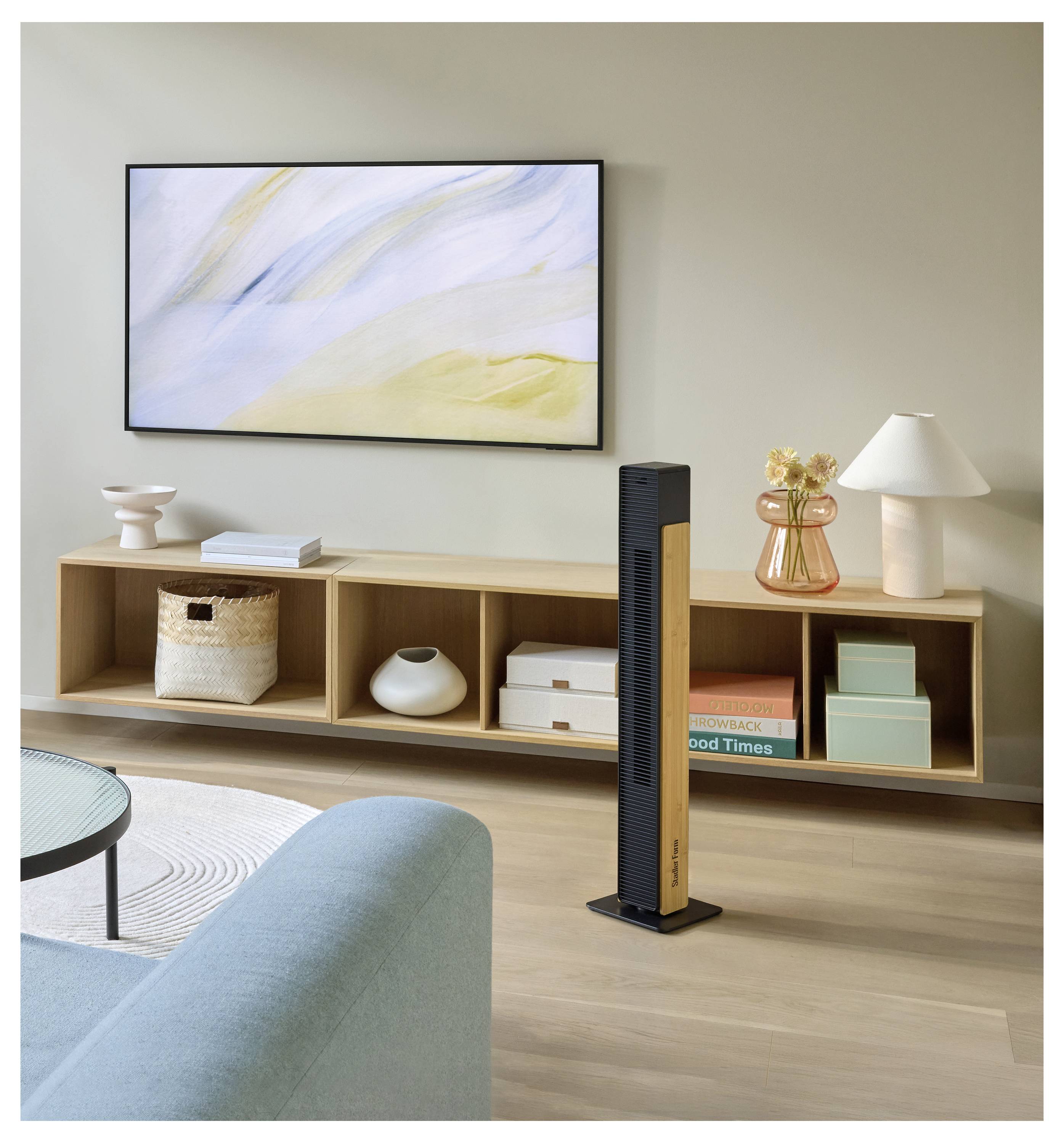Modernes Wohnzimmer mit einem hohen schwarzen Turmventilator, der in der Mitte vor einer niedrigen hölzernen Medienkonsole positioniert ist, unter abstrakter Wandkunst und neben einer Lampe, Büchern und Dekoration.
