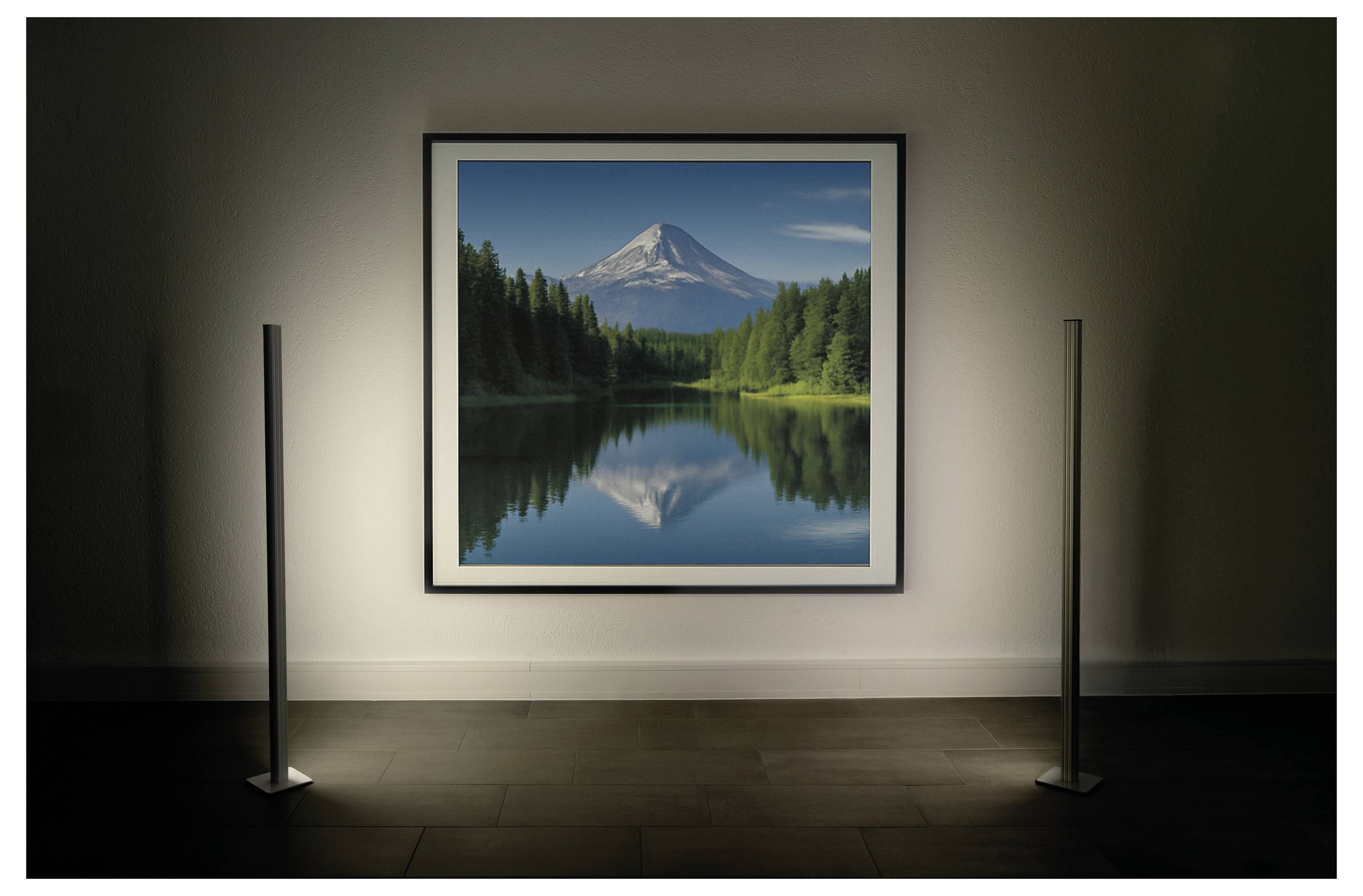 Ein gerahmtes Landschaftsfoto eines schneebedeckten Berges, der sich in einem ruhigen See spiegelt, wird an einer Galeriewand mit Spotlights ausgestellt.