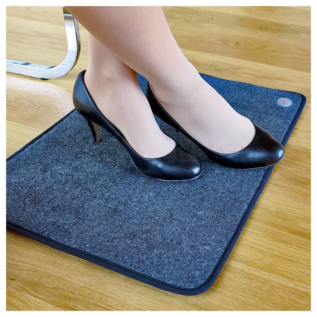 Eine Person, die schwarze High Heels trägt, steht auf einer kleinen rechteckigen Bodenmatte auf einem Holzboden.