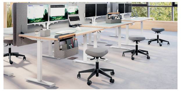 Modernes Open-Space-Büro mit Stehschreibtischen, mehreren Monitoren, Drehstühlen und großen Fenstern mit Blick auf Grünflächen.