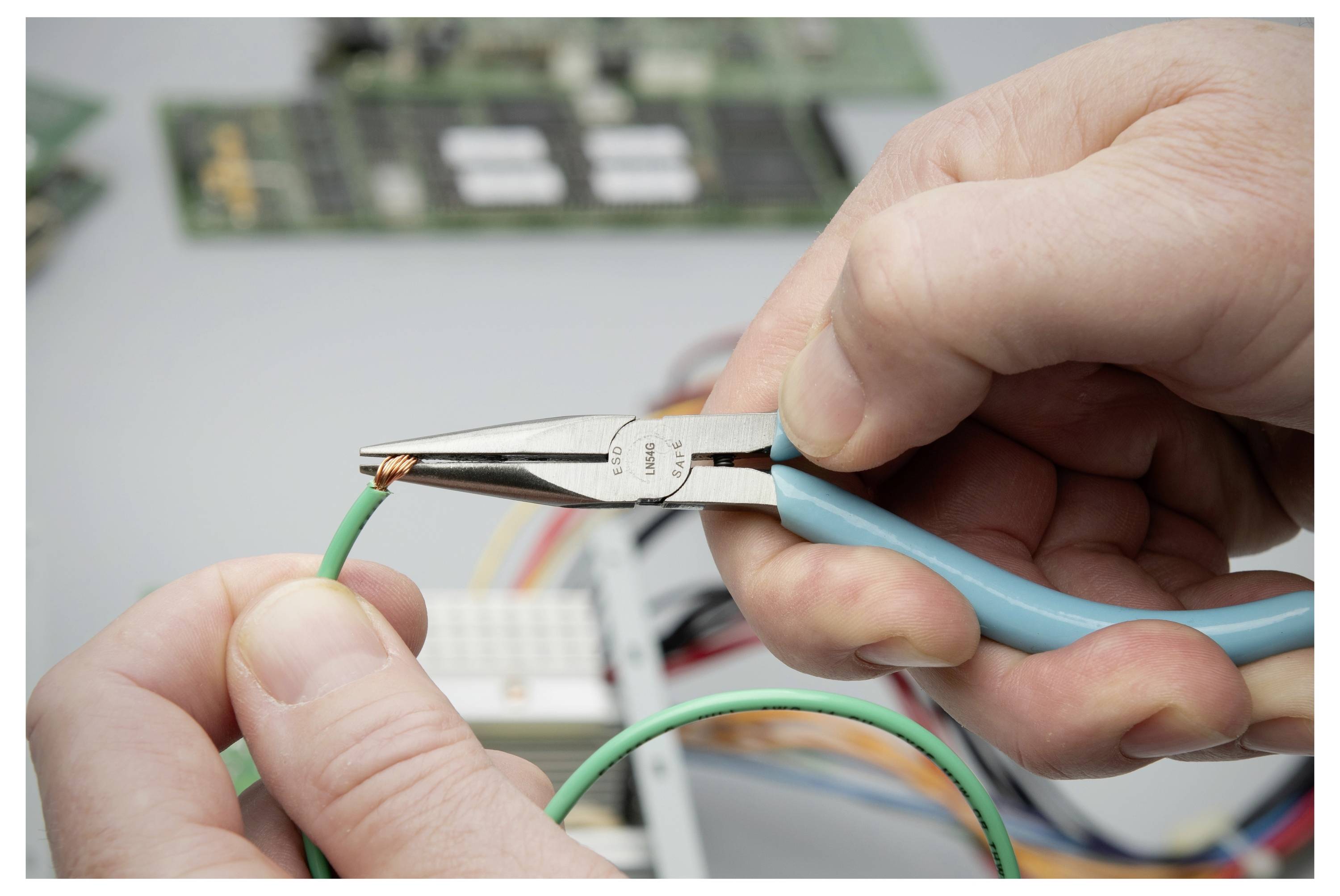 Hände, die eine Zange verwenden, um das Ende eines grünen Drahts während einer Elektronikreparatur oder Verdrahtungsaufgabe abzuisolieren.