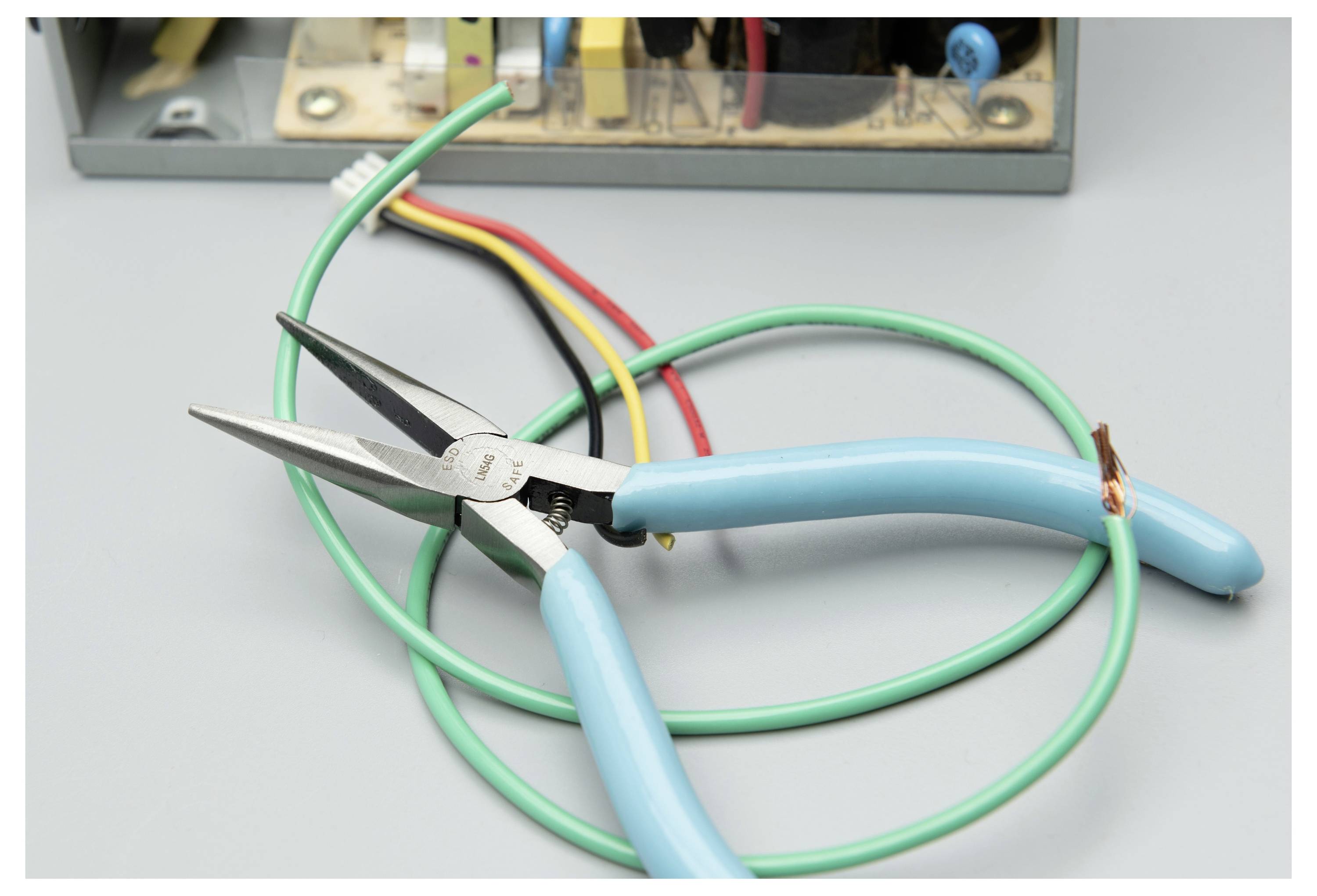 Zange mit blauem Griff, der ein grünes Kabel schneidet, mit roten, gelben und grünen Kabeln auf einer Werkbank.