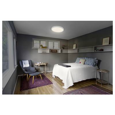 Modernes Schlafzimmer mit einem Bett, einem Sessel, Nachttischen, Wandregalen und großen Fenstern auf der linken Seite, beleuchtet durch eine Deckenleuchte.