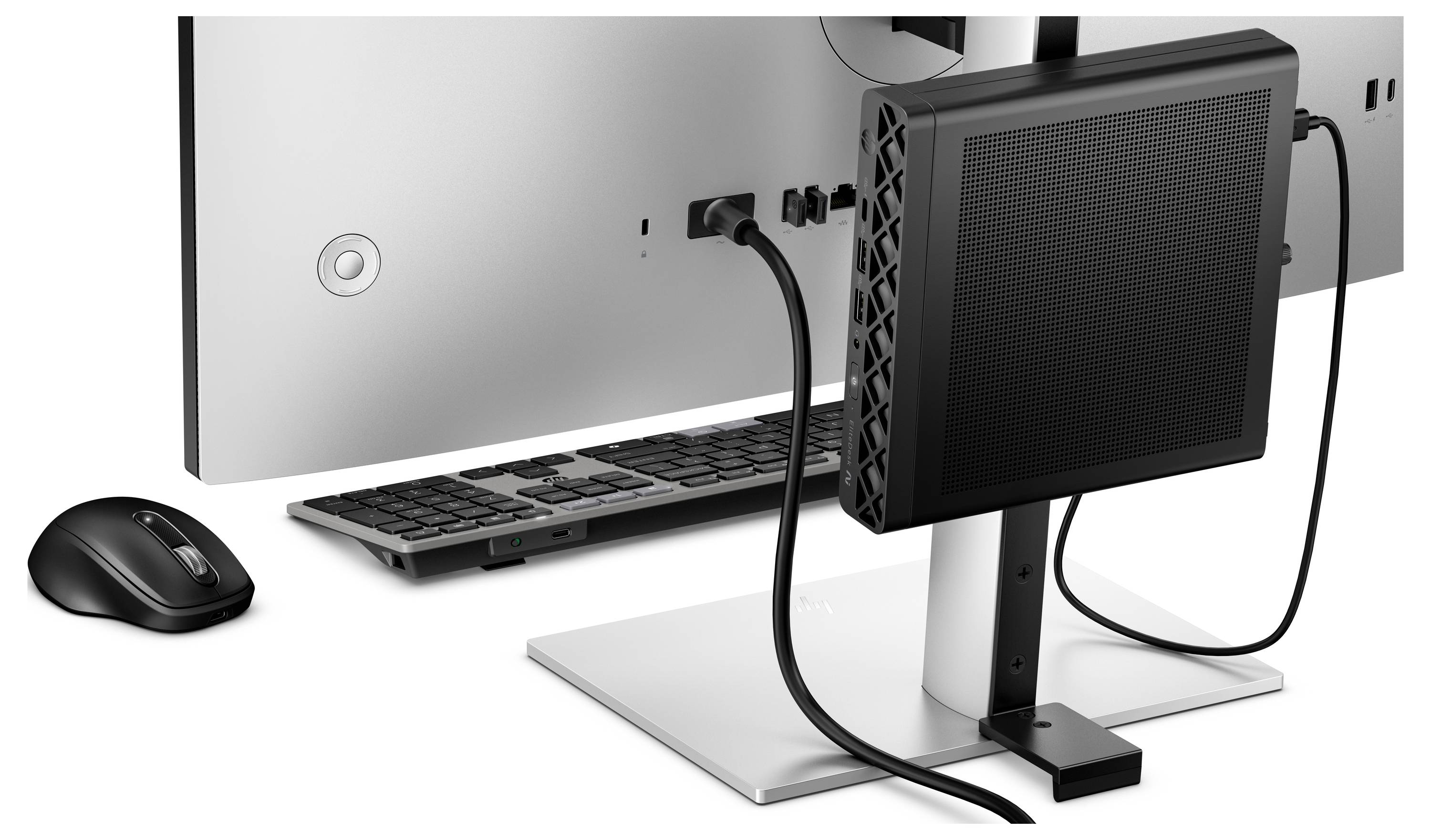 Rückansicht eines Desktop-Computer-Setups mit Monitor, Tastatur, Maus und einem kleinen schwarzen Gerät, das auf dem Ständer montiert ist, mit angeschlossenen Kabeln.