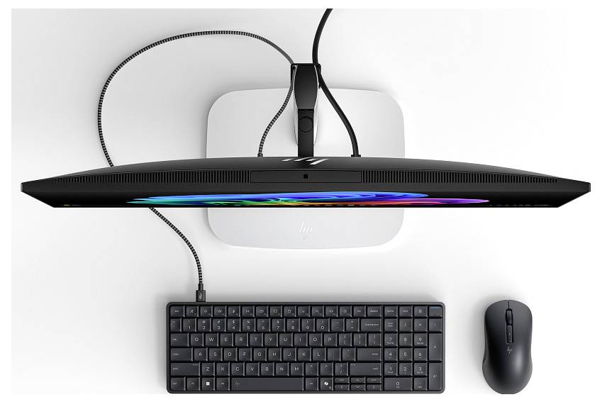 Draufsicht eines Desktop-Setups mit einem großen Monitor auf einem Arm, kabellosen Tastatur und Maus, mit Kabelverbindungen auf einem weißen Schreibtisch.