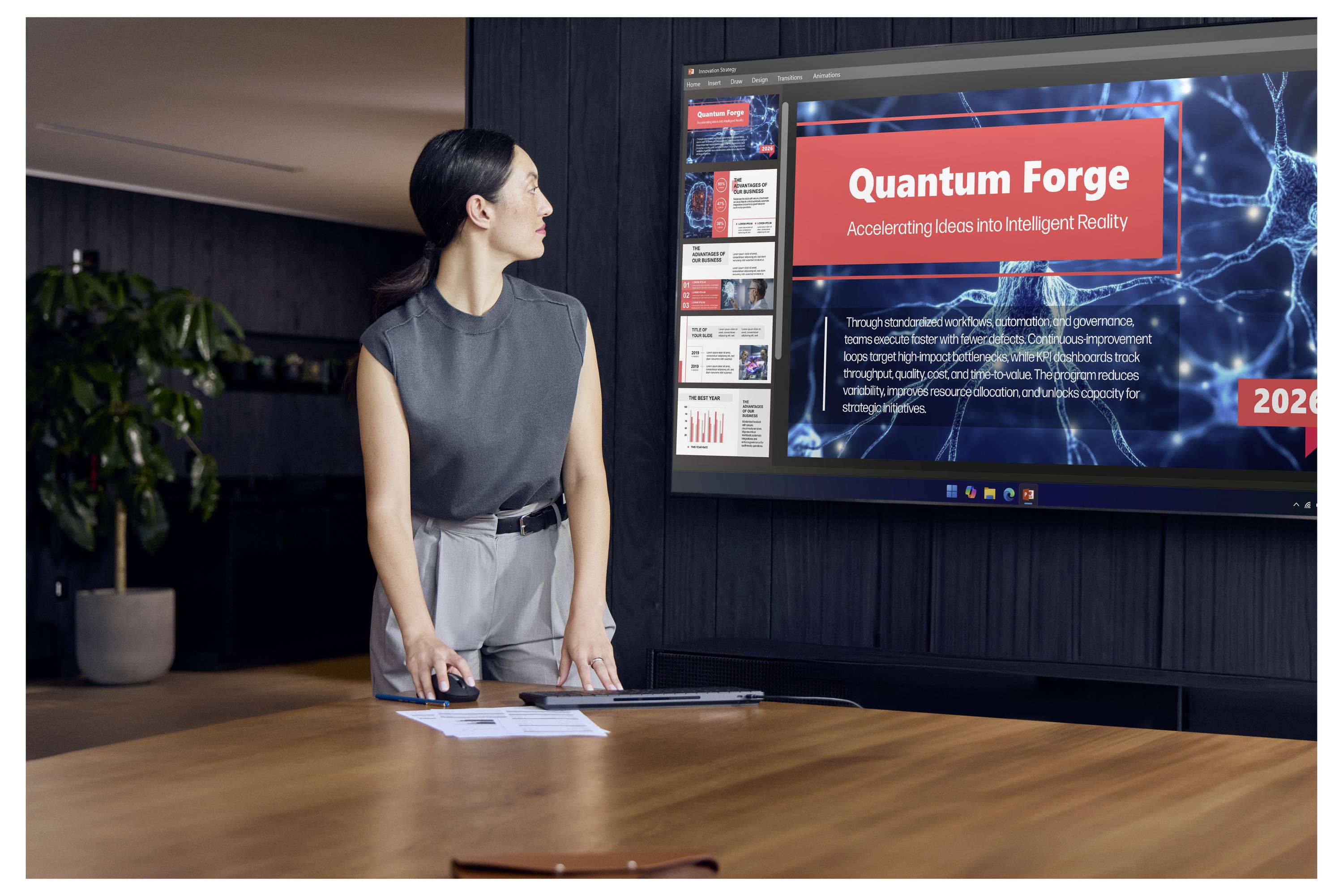 Der Präsentator steht neben einem Konferenzbildschirm, auf dem eine Folie mit dem Titel "Quantum Forge" und dem Untertitel "Accelerating Ideas into Intelligent Reality" sowie einer Beschriftung von 2024 angezeigt wird.