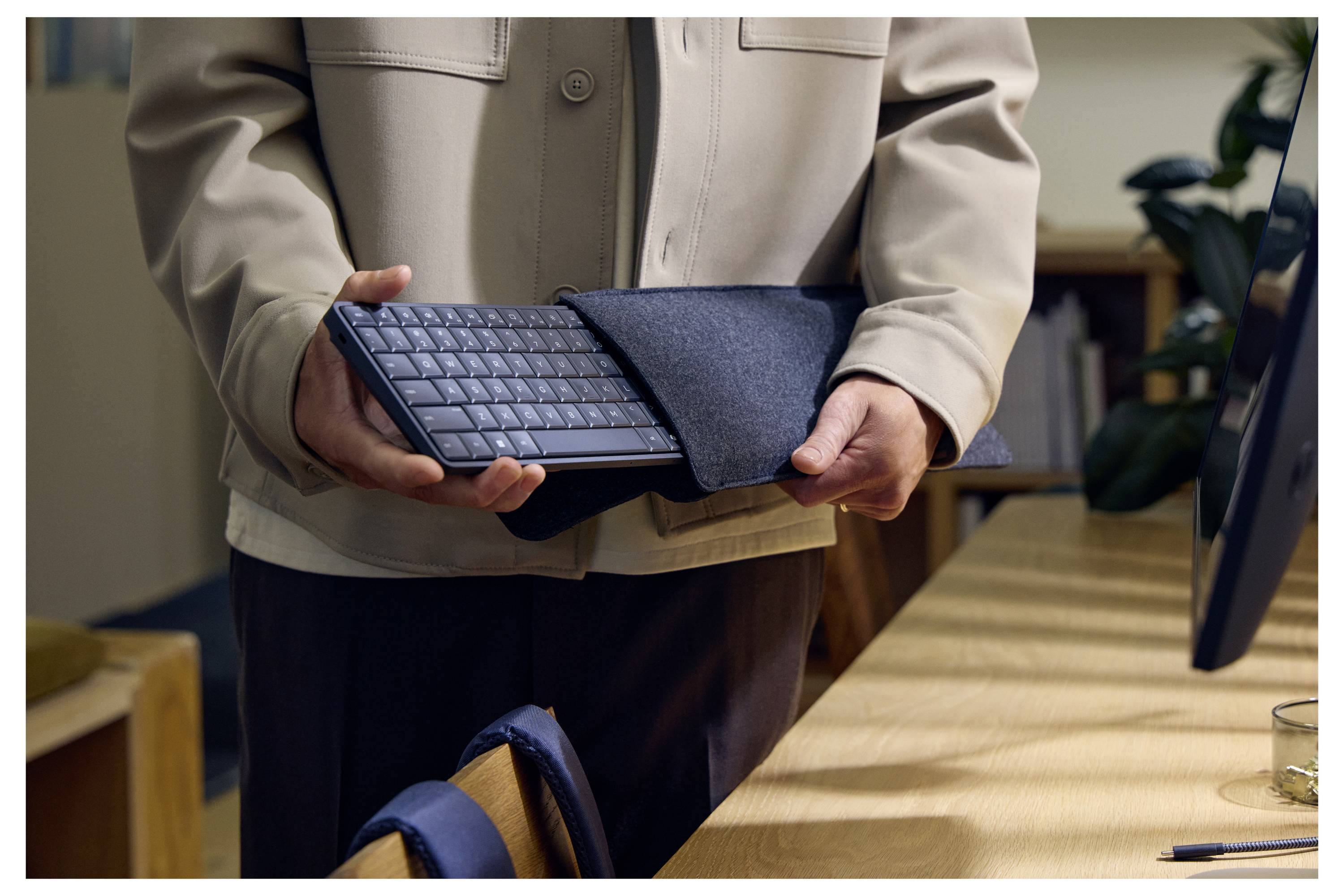 Eine Person hält ein Tablet mit einer Tastaturhülle an einem Schreibtisch in einer Büroumgebung.