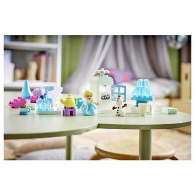 Spielbausteine und kleine Figuren, die auf einem Spieltisch in einem Kinderzimmer angeordnet sind, mit einem Miniaturhaus und Möbelstücken.