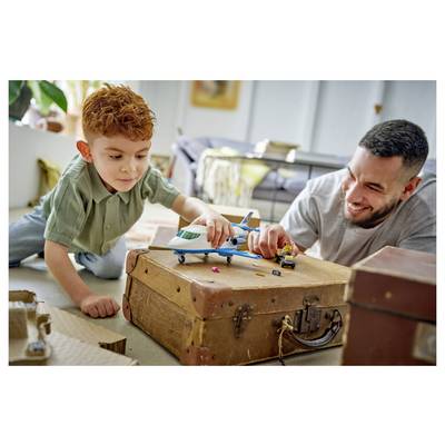 Kleiner Junge und lächelnder Mann spielen mit einem Hubschrauber-Spielzeug und einer Figur auf einem Koffer und sitzen zu Hause auf dem Boden.