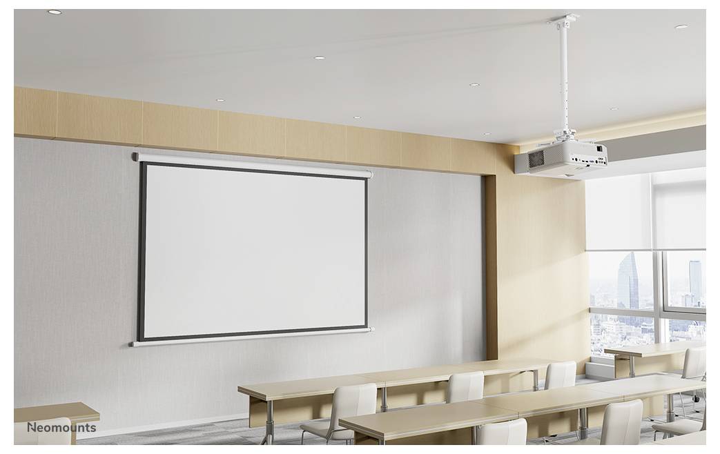 Leeres Klassenzimmer mit einer leeren herunterziehbaren Projektionsleinwand, an der Decke montiertem Projektor und Reihen von Tischen und Stühlen neben einem Fenster.