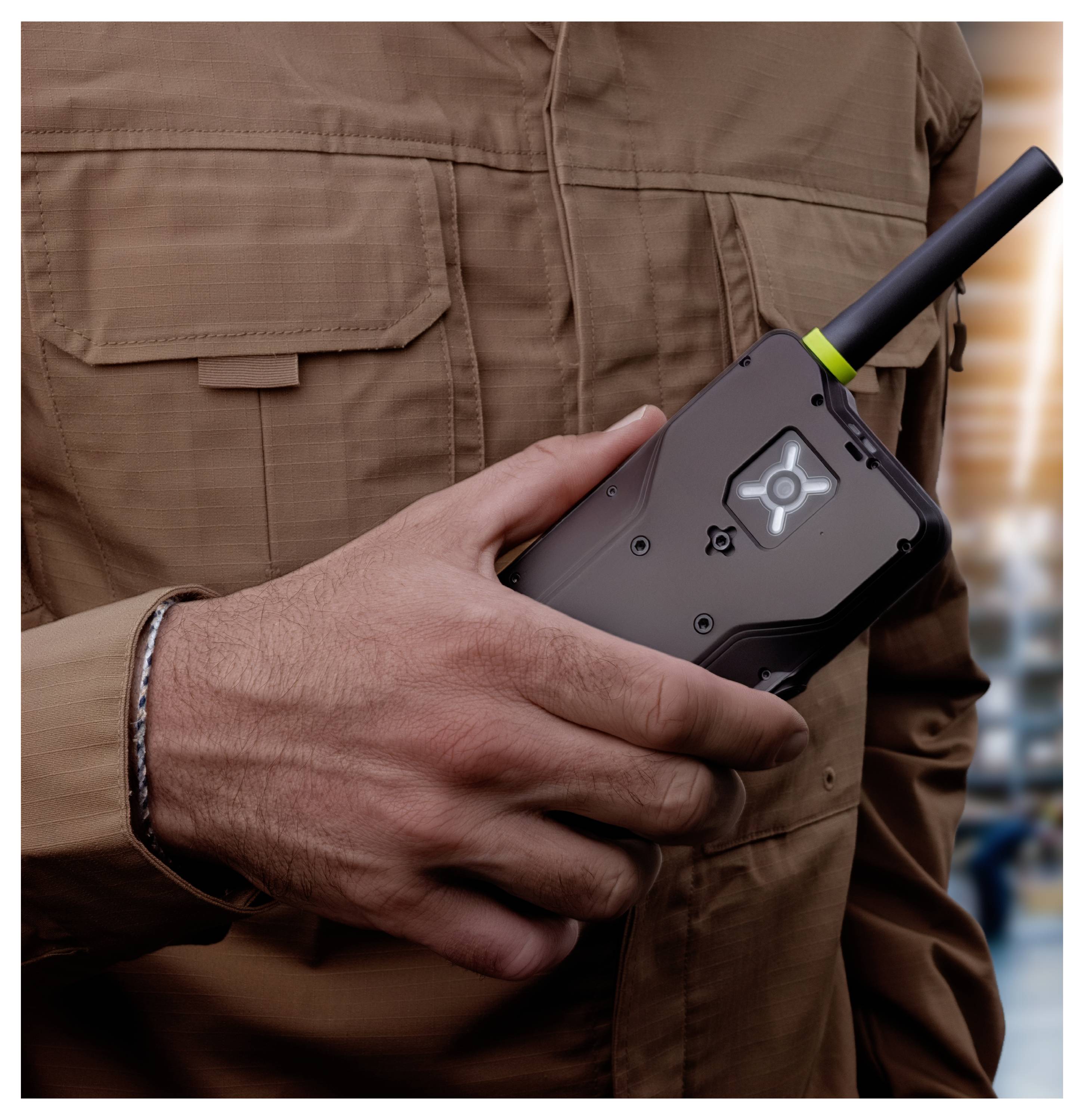 Person in a brown jacket holding a black handheld two-way radio with antenna and illuminated screen.<br><br>Personen in einer braunen Jacke, die ein schwarzes tragbares Funkgerät mit Antenne und leuchtendem Bildschirm halten.