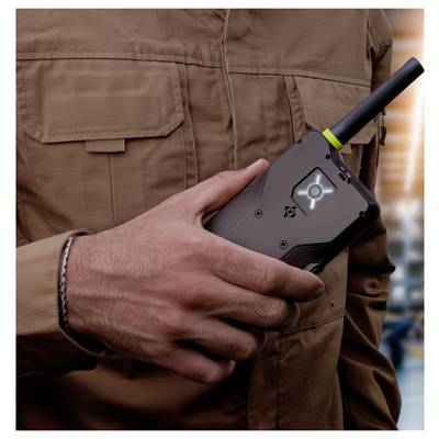 Person in a brown jacket holding a black handheld two-way radio with antenna and illuminated screen.<br><br>Personen in einer braunen Jacke, die ein schwarzes tragbares Funkgerät mit Antenne und leuchtendem Bildschirm halten.