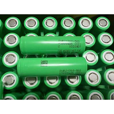 Grüne zylindrische Batterien in Reihen gestapelt, mit zwei beschrifteten Zellen, die oben quer angeordnet sind und auf Speicherung oder Überprüfung von wiederaufladbaren Batterien hindeuten.