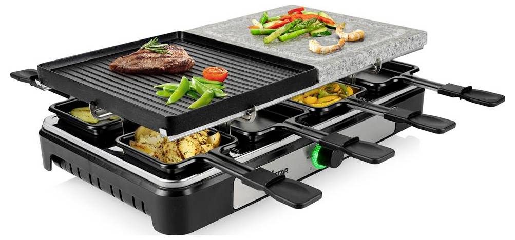 Tisch-Raclette-Grill mit zwei Grillplatten und Lebensmittelschalen, auf dem Steak, Gemüse, Garnelen und Kartoffeln gegart werden; grüner Temperaturreglerschalter sichtbar.