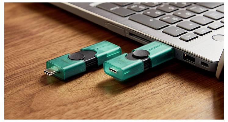 Zwei türkisfarbene USB-Speichersticks, die an einen Laptop auf einem Holzschreibtisch angeschlossen sind, einer in den USB-Anschluss gesteckt.