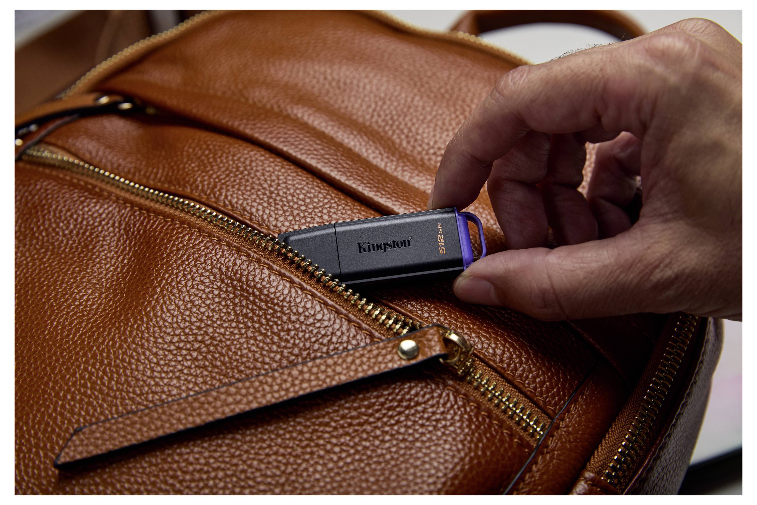 Die Hand führt einen Kingston USB-Stick in die Reißverschlussöffnung einer braunen Ledertasche ein.