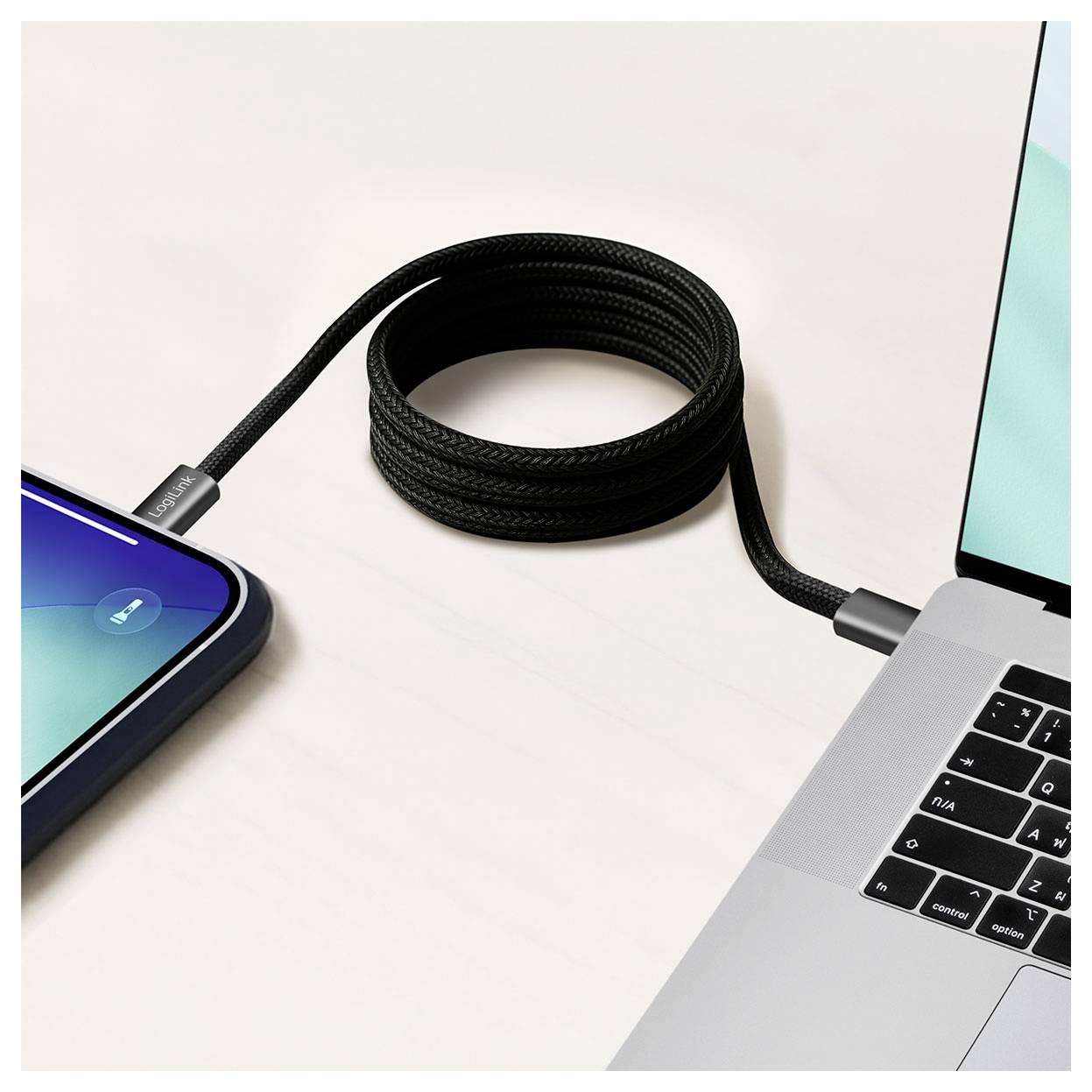 Schwarzes Kabel, das ein Smartphone und einen Laptop verbindet, mit dem Kabel, das in der Mitte aufgerollt ist, während die Geräte geladen werden oder Daten übertragen.