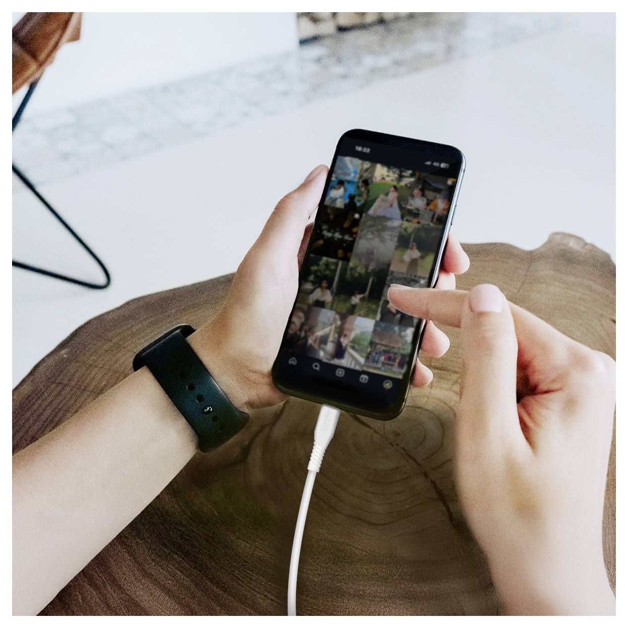 Hände, die ein Smartphone mit einer offenen Fotogalerie verwenden, ein Finger tippt auf den Bildschirm, während das Telefon auf einem Tisch aufgeladen wird.