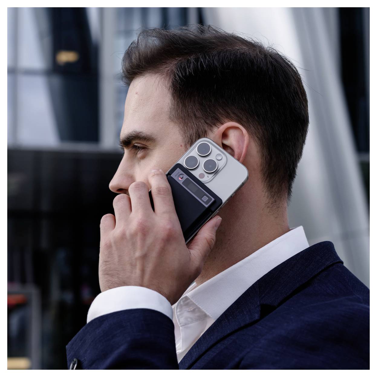 Ein Mann in einem marineblauen Anzug hält sich ein Smartphone ans Ohr und telefoniert im Freien in der Nähe eines modernen Gebäudes.