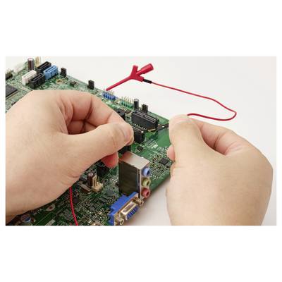 Hände mit roten Prüfleitungen, die eine Computermainplatine prüfen, deuten auf elektronische Fehlersuche oder Reparatur hin.