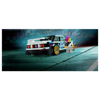 Lego-ähnlicher Sportwagen mit goldenen Rädern und eine Minifigur, die daneben auf einem blaugrün beleuchteten Studioboden steht.