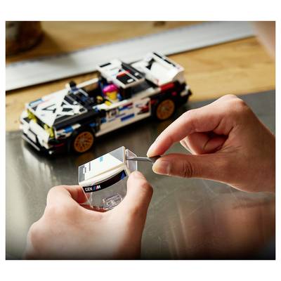 Kind, das ein weiß-schwarzes Spielzeugrennwagen mit einem transparenten Teil zusammenbaut, mit dem teilweise gebauten Auto auf einem Tisch im Hintergrund.