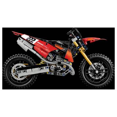 Seitenansicht eines roten LEGO-Ducati-DesertX-ähnlichen Geländemotorrad-Modells mit sichtbarem Motor, Aufhängung und Knobby-Reifen auf schwarzem Hintergrund.