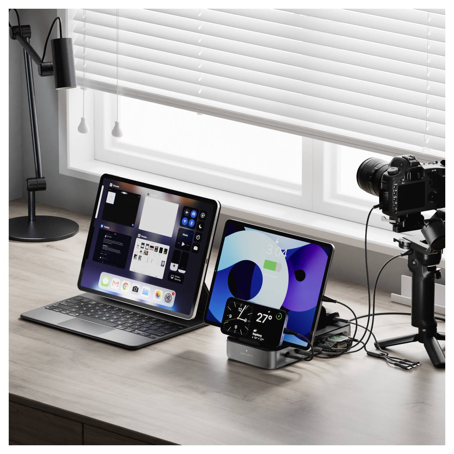 Schreibtischaufbau mit einem Laptop, Tablet und einer Kamera auf einem Stativ, die einen Streaming- oder Content-Creation-Arbeitsplatz neben einem Fenster zeigen.