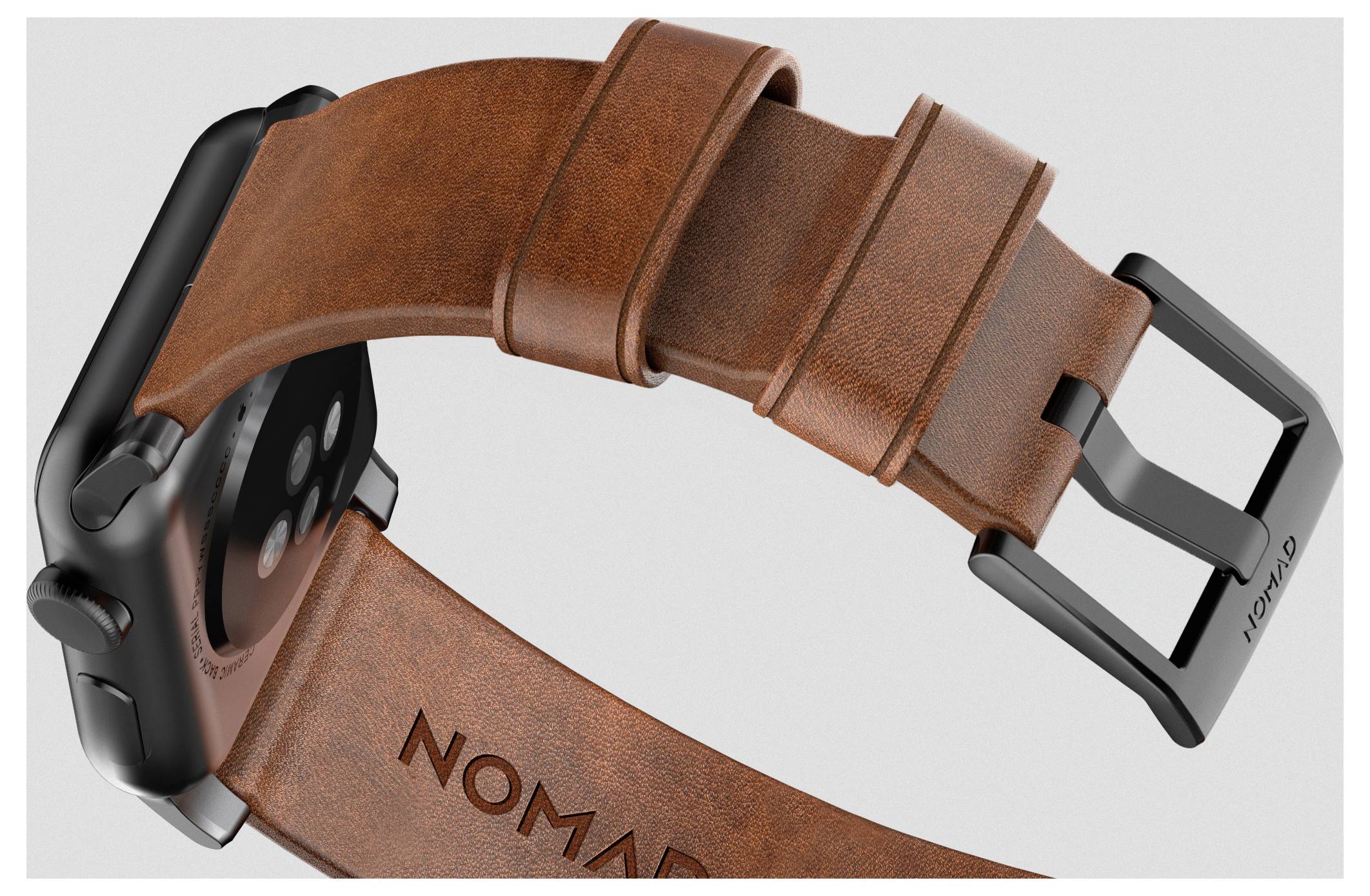 Nahaufnahme einer Smartwatch mit braunem Lederarmband und schwarzer Metallschnalle, auf der das Logo "NOMAD" auf dem Armband zu sehen ist.
