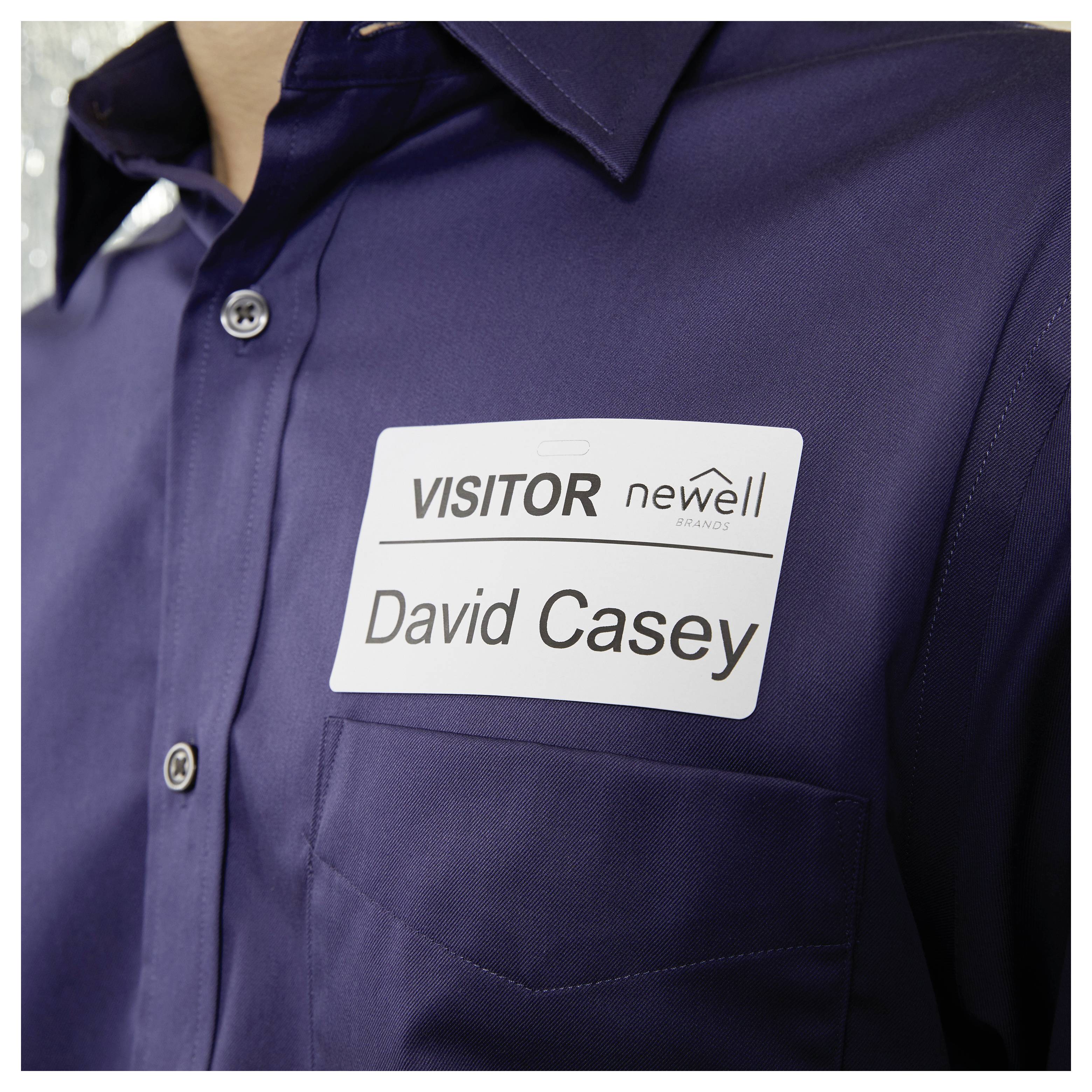 Nahaufnahme einer Person in einem dunkelblauen Hemd mit einem Besucherausweis, auf dem "VISITOR" und "David Casey" steht.
