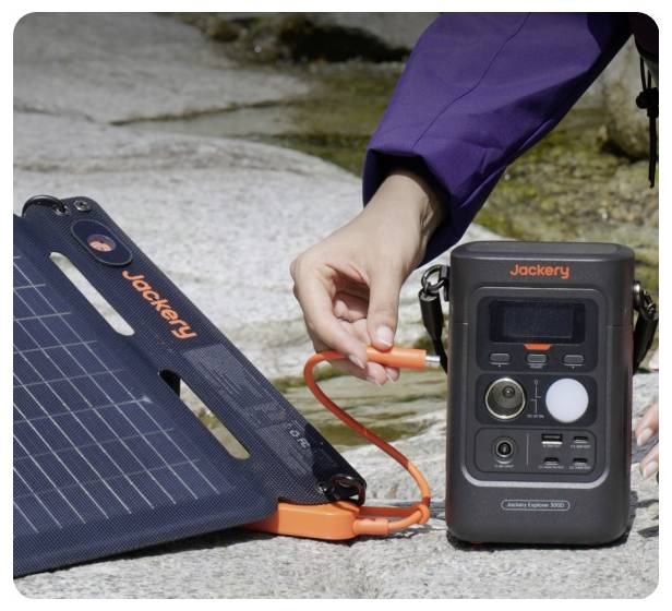 Eine Hand steckt ein orangefarbenes Kabel eines Jackery-Solarpanels in eine tragbare Jackery-Powerstation, die sich im Freien auf Fels befindet.