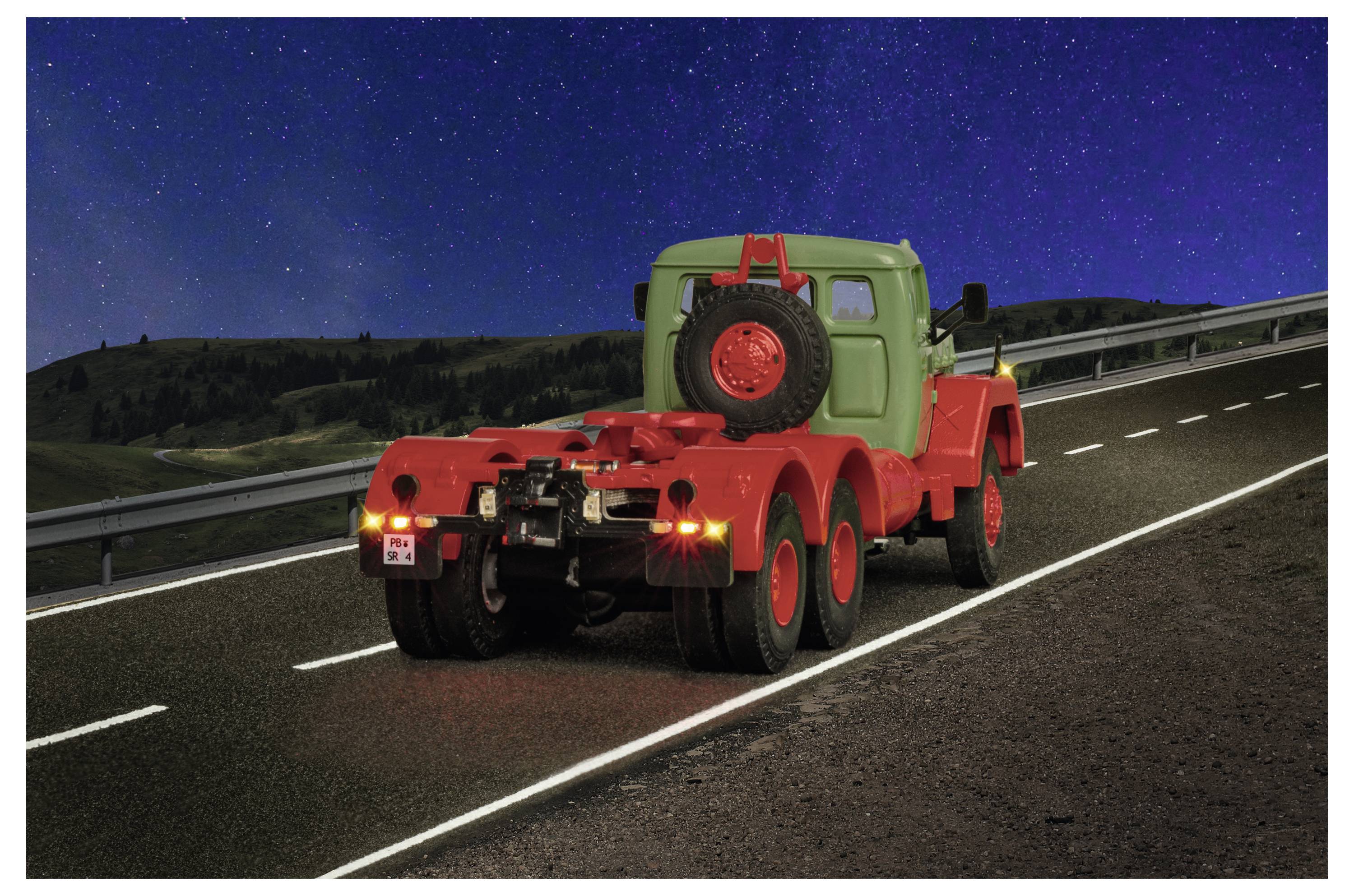 Roter Spielzeugkranstwagen mit einem Ersatzreifen auf der Rückseite fährt nachts auf einer Autobahn unter einem Sternenhimmel.