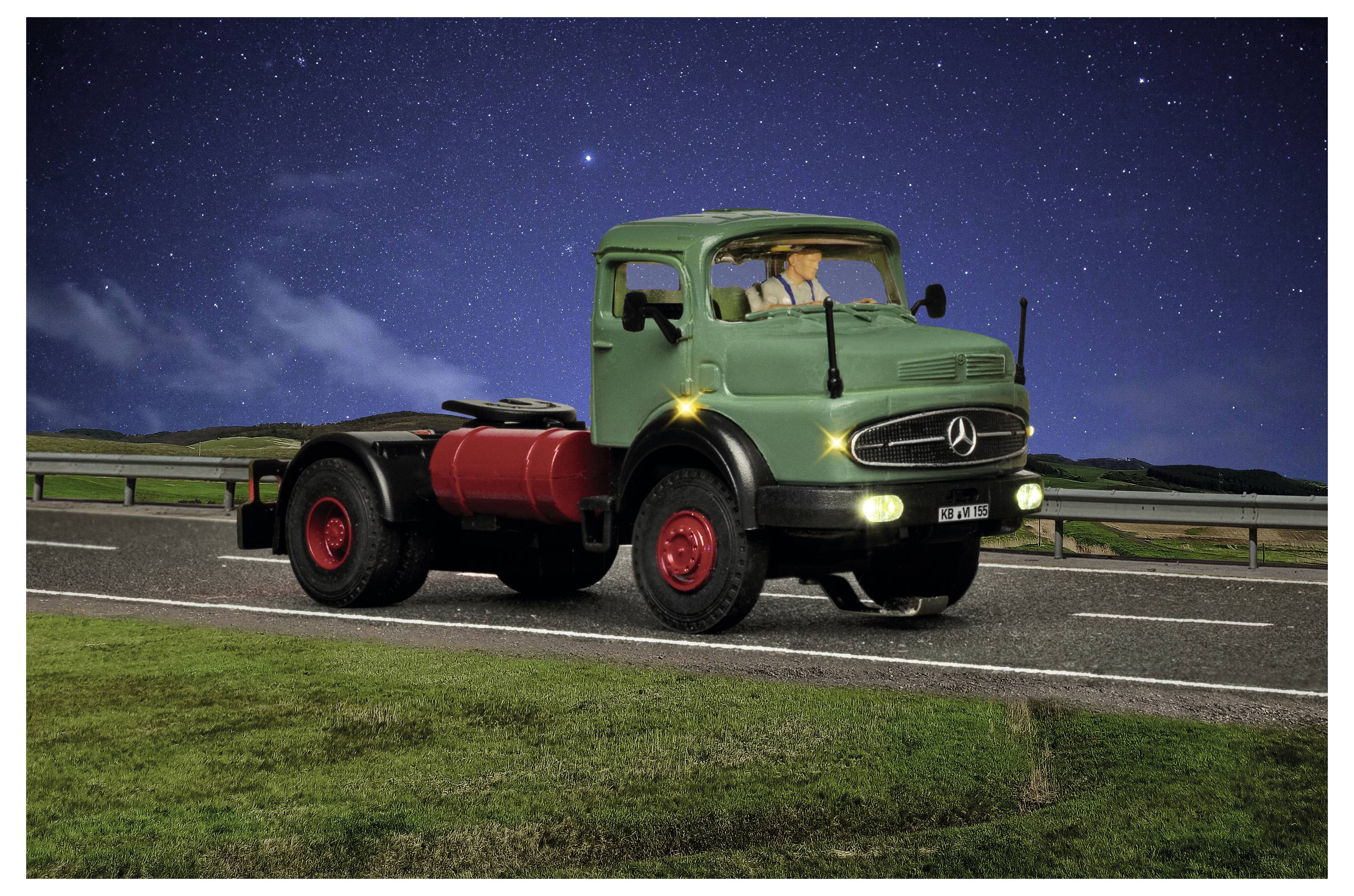 Vintage grüner Mercedes-Lastwagen, der nachts am Straßenrand geparkt ist, mit eingeschalteten Scheinwerfern und einem Sternenhimmel im Hintergrund.