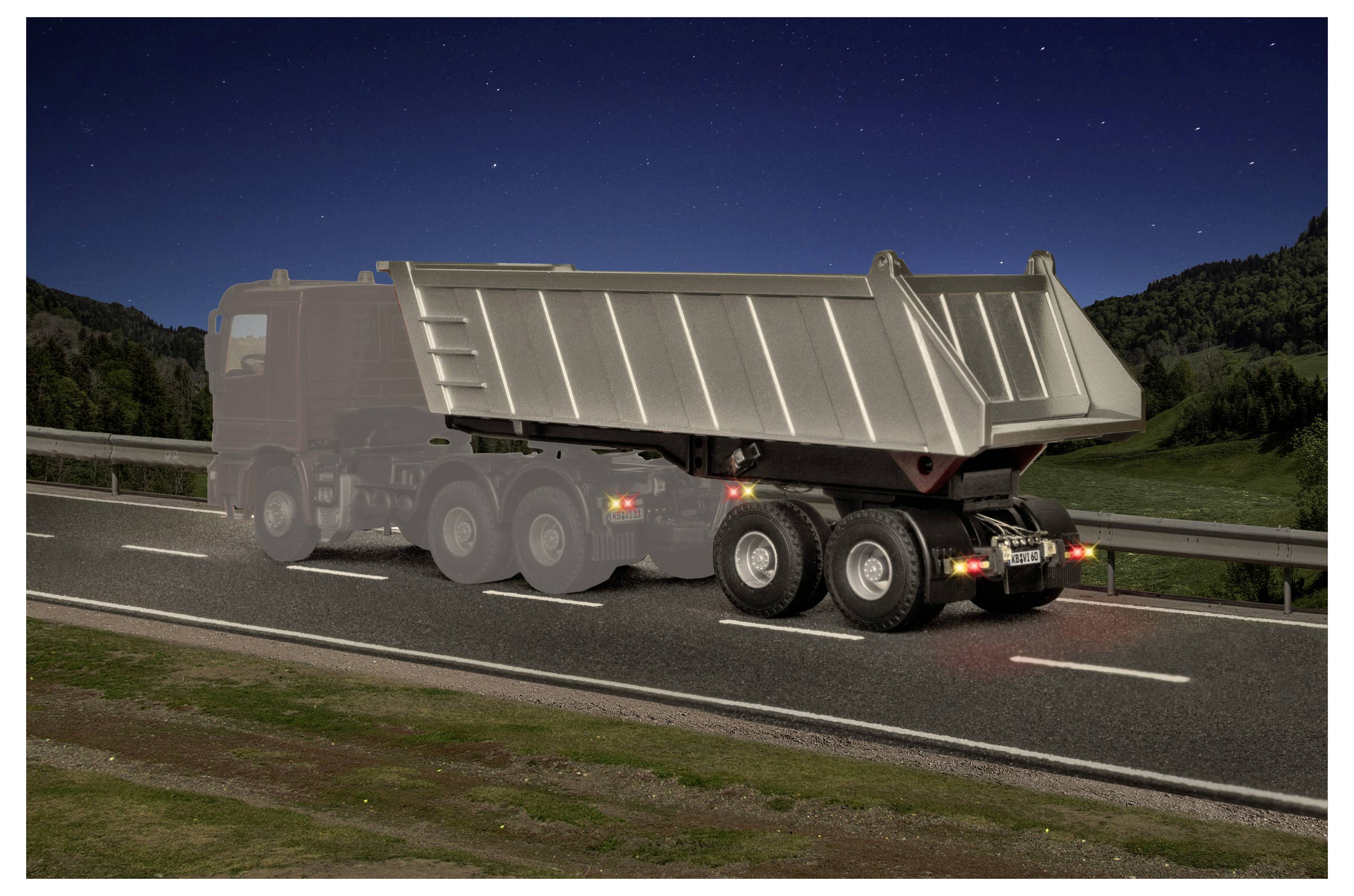 Kipplastwagen fährt nachts auf einer Autobahn und wird von hinten gezeigt, mit angehobenem Ladefläche und sichtbaren Rückleuchten.