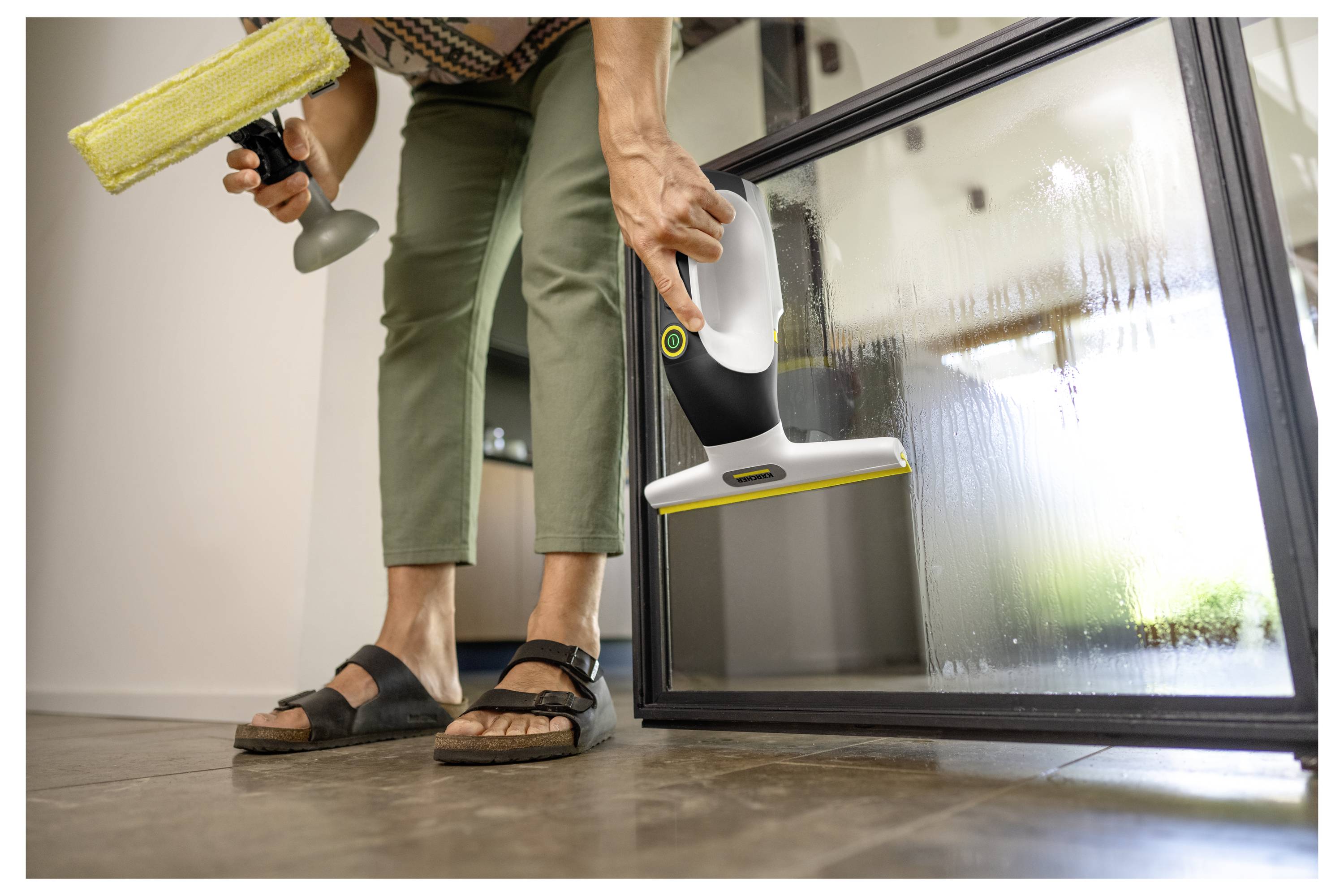 Person mit einem Fensterabzieher und einer Sprühflasche, die eine große Glastür im Innenbereich reinigt.