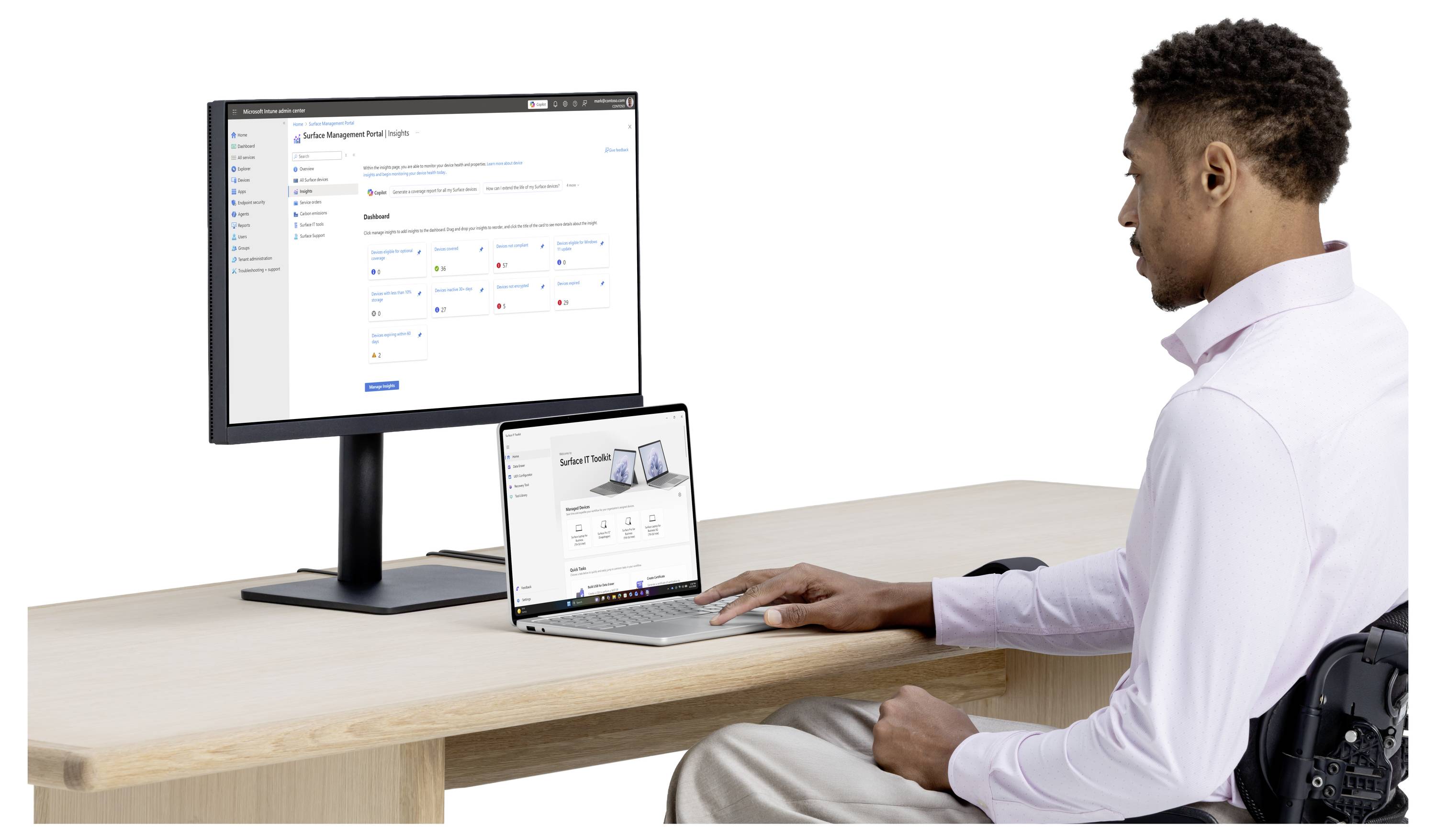Ein Mann im Rollstuhl nutzt einen Laptop neben einem externen Monitor, der ein Website-Dashboard anzeigt, während er an einem Schreibtisch arbeitet.