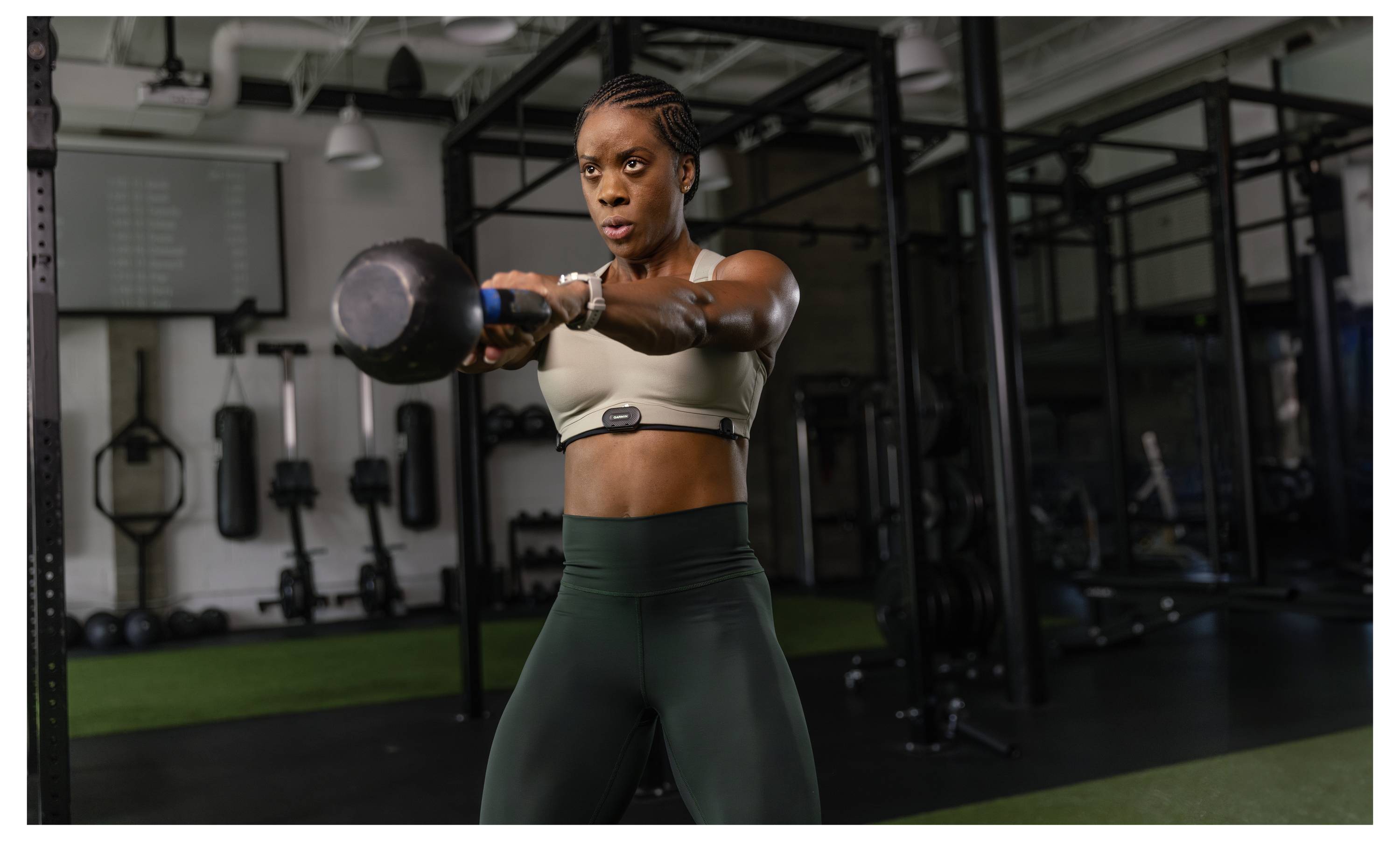 Frau im Fitnessstudio, die während einer Krafttrainingsübung eine Kettlebell gerade vor sich hält.