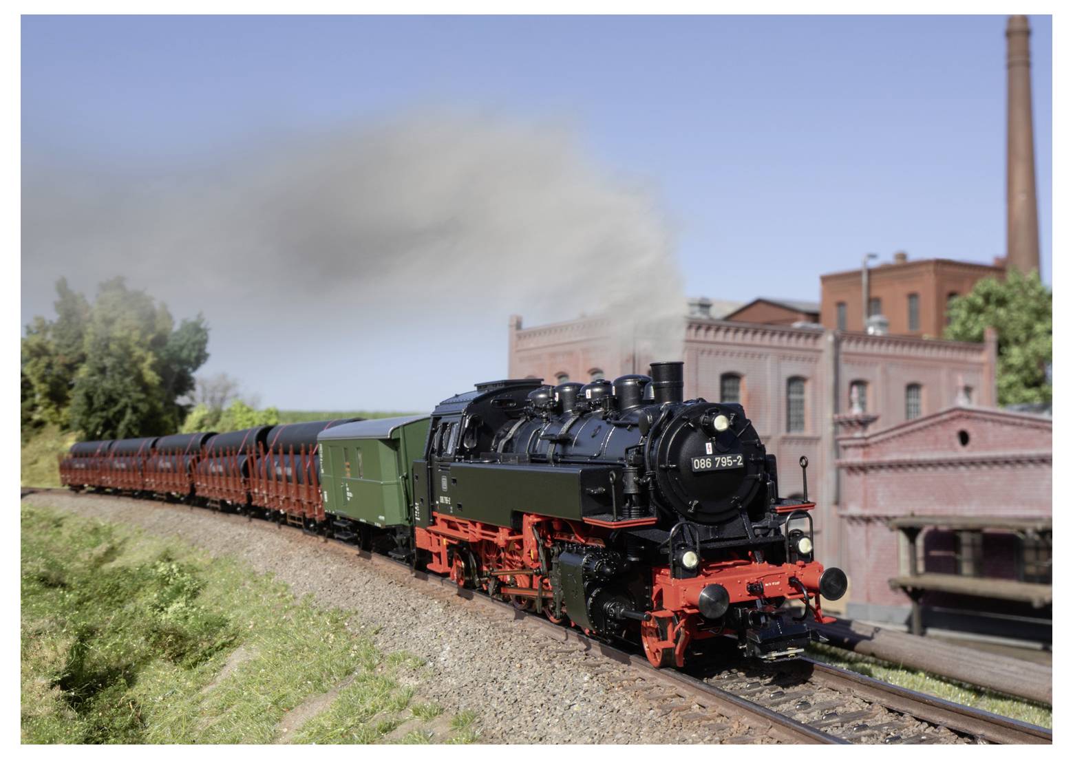 Eine Dampflokomotive, die einen langen Personenzug um eine Kurve zieht, mit aufwallendem Rauch und einem Industrieziegelgebäude im Hintergrund.
