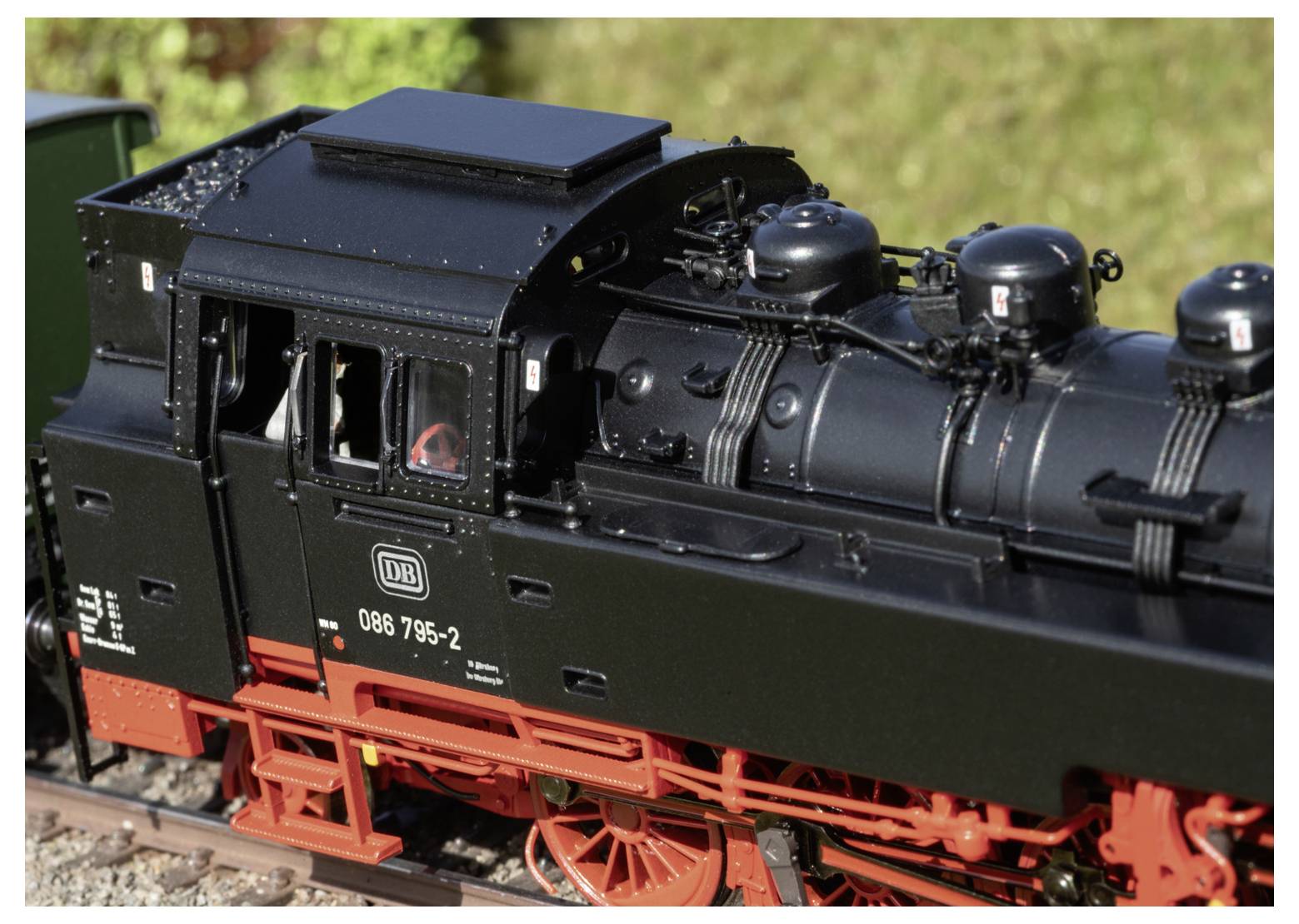 Schwarze modellbau-dampflokomotive mit roten rädern auf gleis im freien, seitenansicht zeigt die kabine und den kessel.