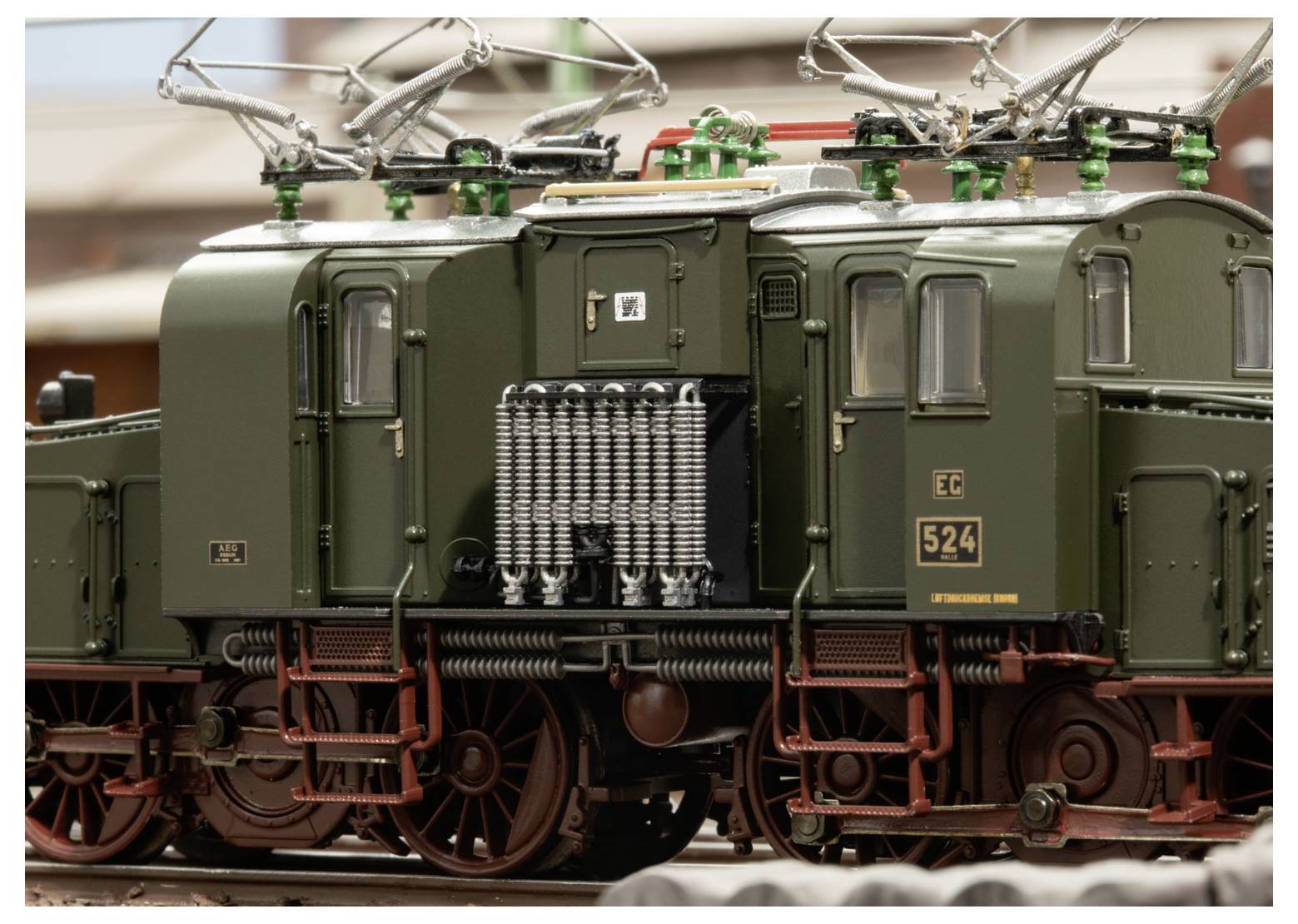 Nahaufnahme eines olivgrünen Elektrolokomotivmodells mit Dachstromabnehmer und detaillierter Seitenmechanik, drinnen auf einer Ausstellung gezeigt.