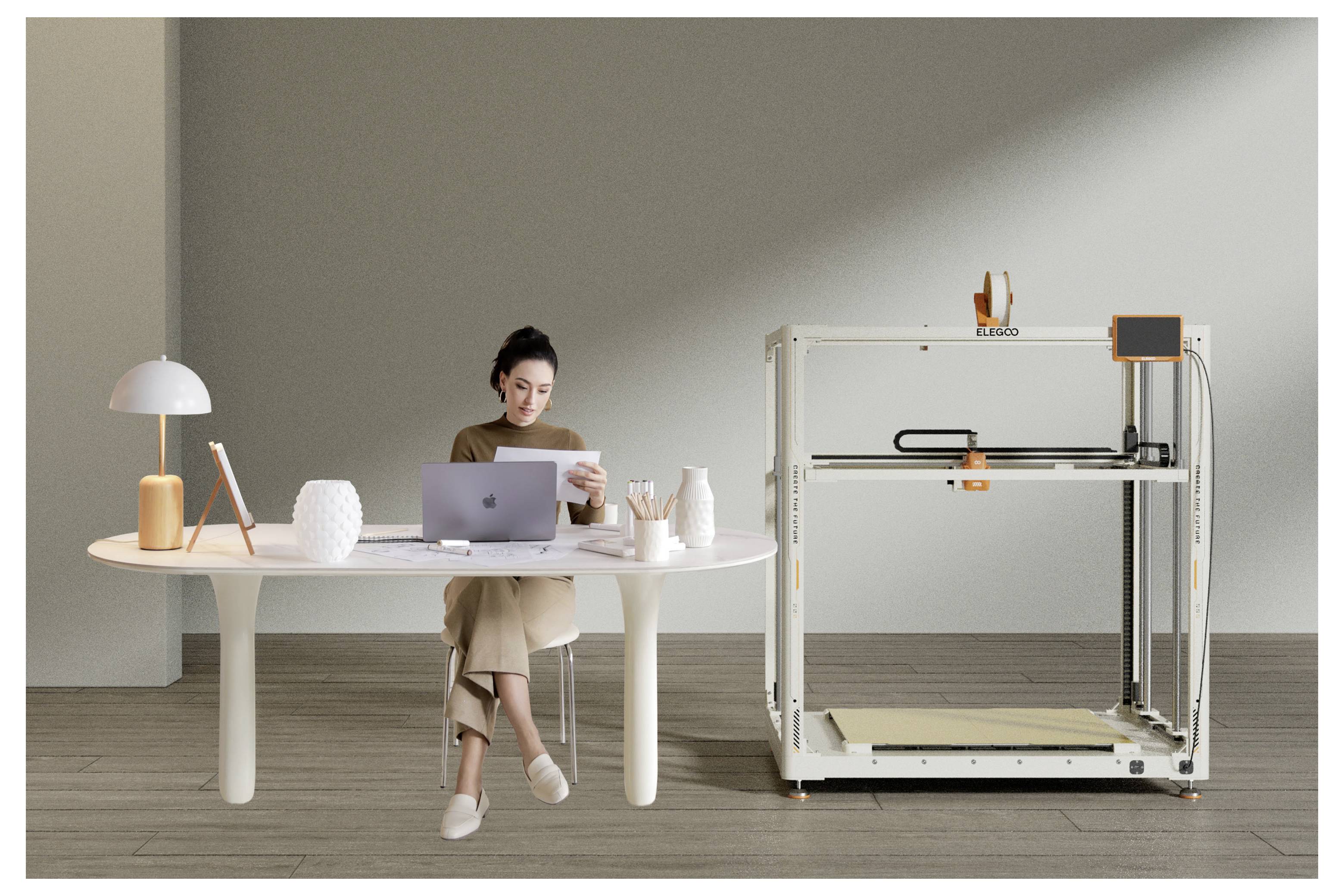 Frau, die an einem Tisch sitzt, einen Laptop benutzt und ein Papier neben einem großen 3D-Drucker in einem minimalistischen Raum liest.