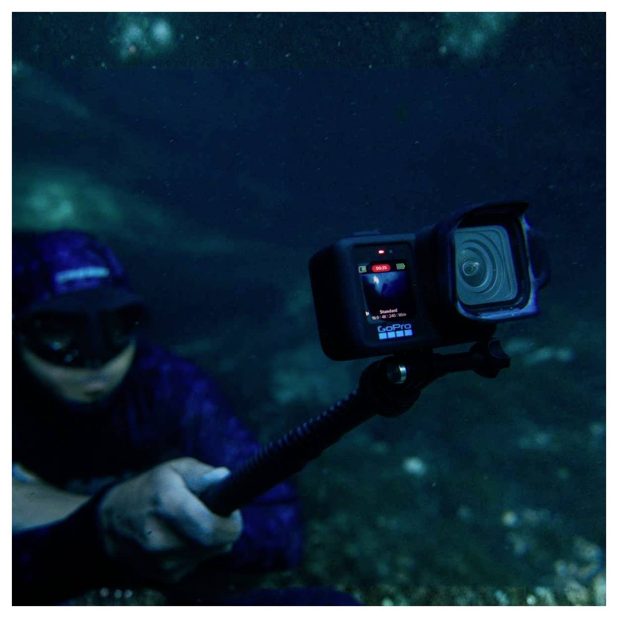 Unterwassertaucher, der eine GoPro-Kamera auf einem Selfie-Stick hält, wobei die Kamera in dunkelblauem Wasser nach außen gerichtet ist.