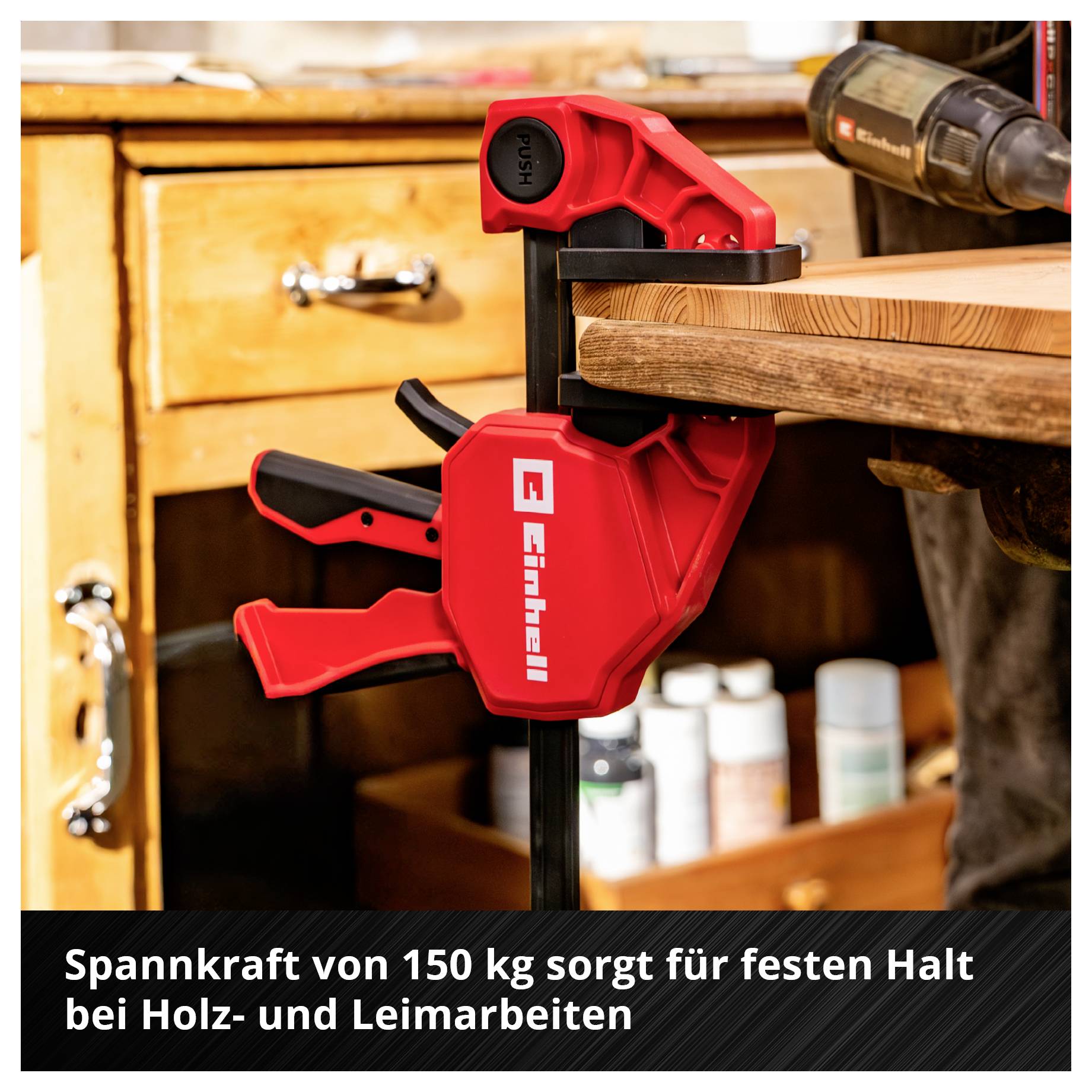Rote Schraubzwinge hält eine Holzplatte auf der Werkbank fest; im Bildtext steht: 'Spannkraft von 150 kg sorgt für festen Halt bei Holz- und Leimarbeiten'.