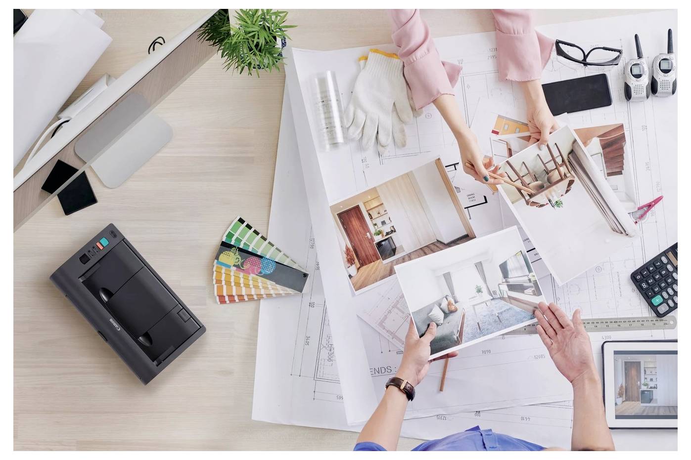 Draufsicht von Architekten, die Grundrisse überprüfen, Innenarchitektur-Fotos und Farbmuster auf einem Schreibtisch mit Werkzeugen und einem Drucker studieren.