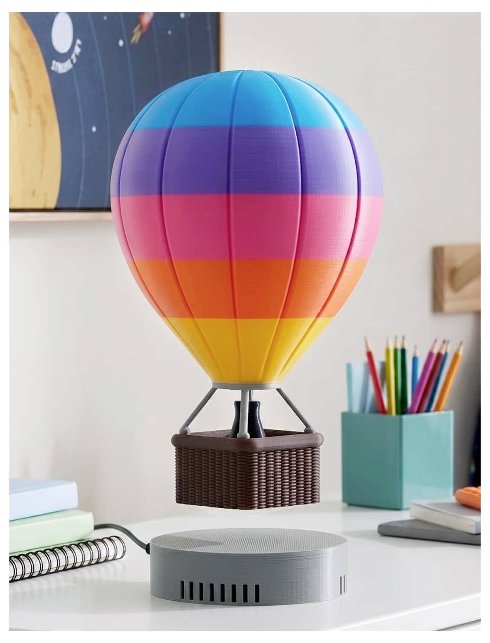 Eine bunte Heißluftballonformige Lampe dekoriert einen Schreibtisch neben Stiften und Notizbüchern, mit einem runden grauen Smart Speaker davor.